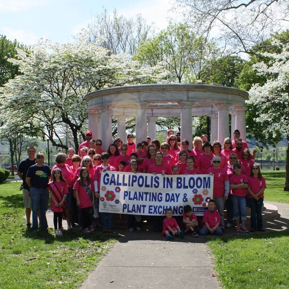 Volunteers in pink shirts holding a Gallipolis in Bloom Planting Day banner in City Park