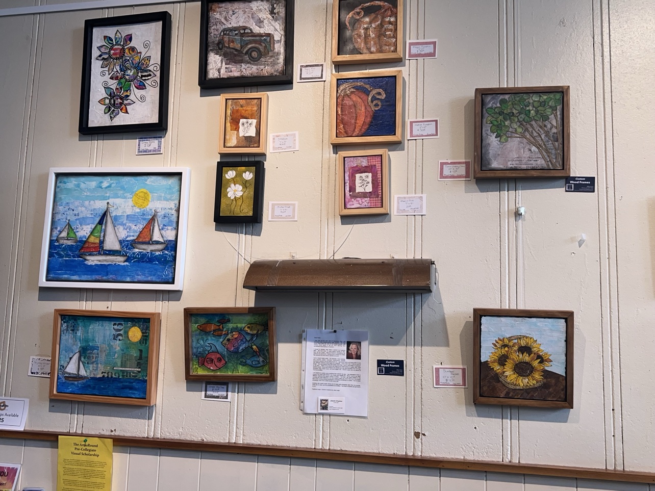 Mixed-media pieces, sailboats, pumpkins and sunflowers, share a wall near the ArtsaRound scholarship display.