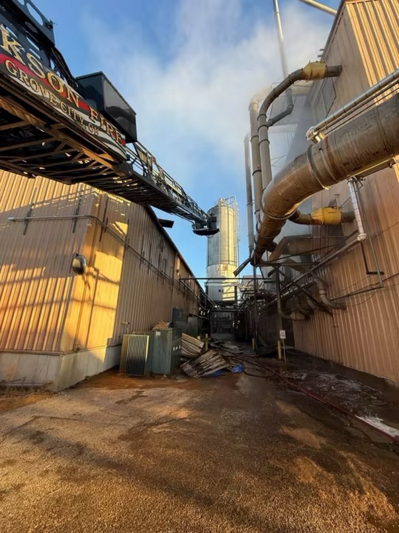 A Jackson Township aerial ladder reaches over the plant toward the silo as smoke rises.