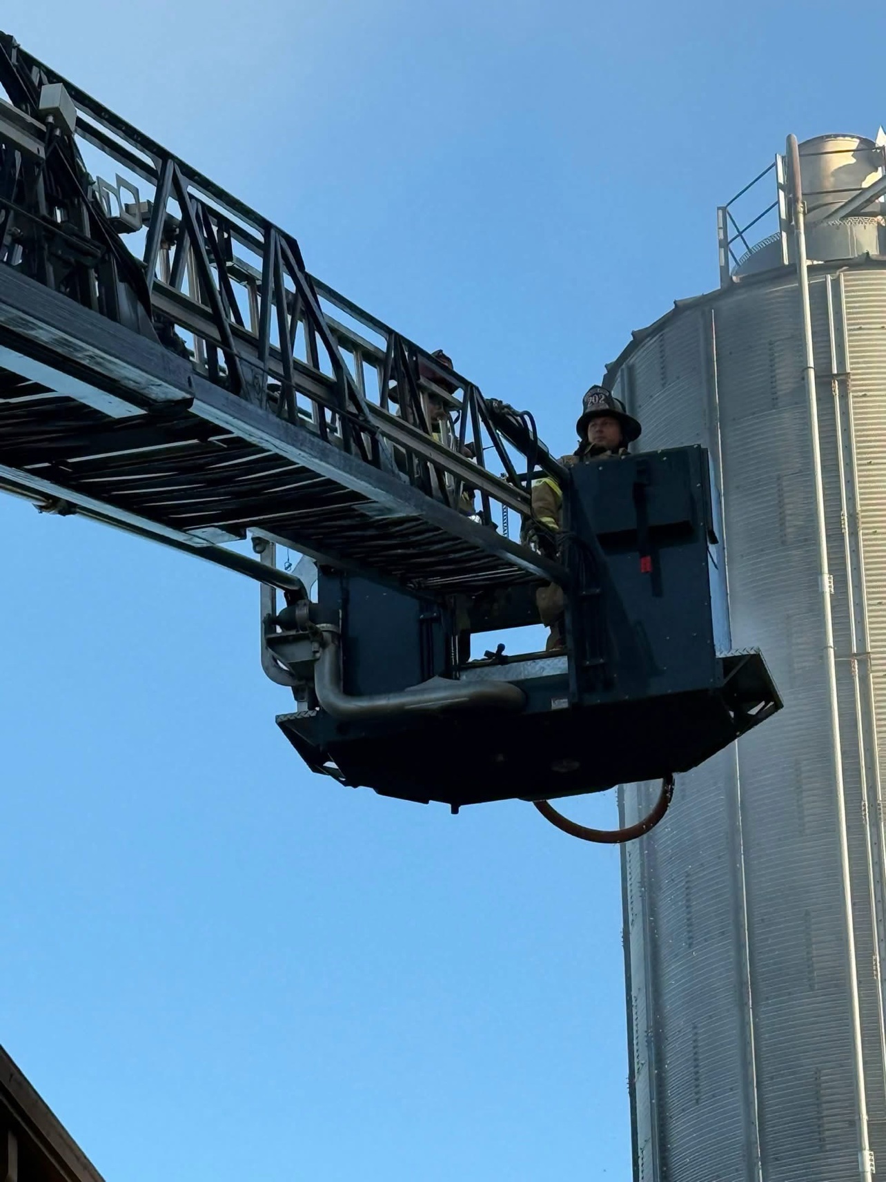 A firefighter rides the aerial bucket high beside the silo.