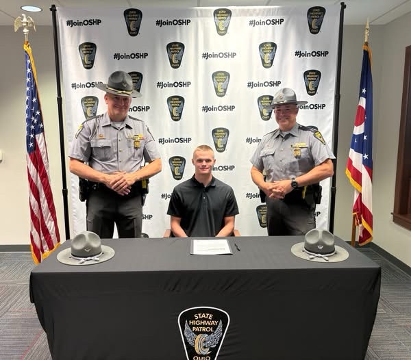A cadet seated at the signing table between two Ohio State Highway Patrol troopers