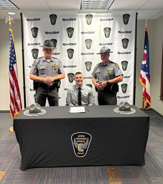 A cadet seated at the signing table between two Ohio State Highway Patrol troopers