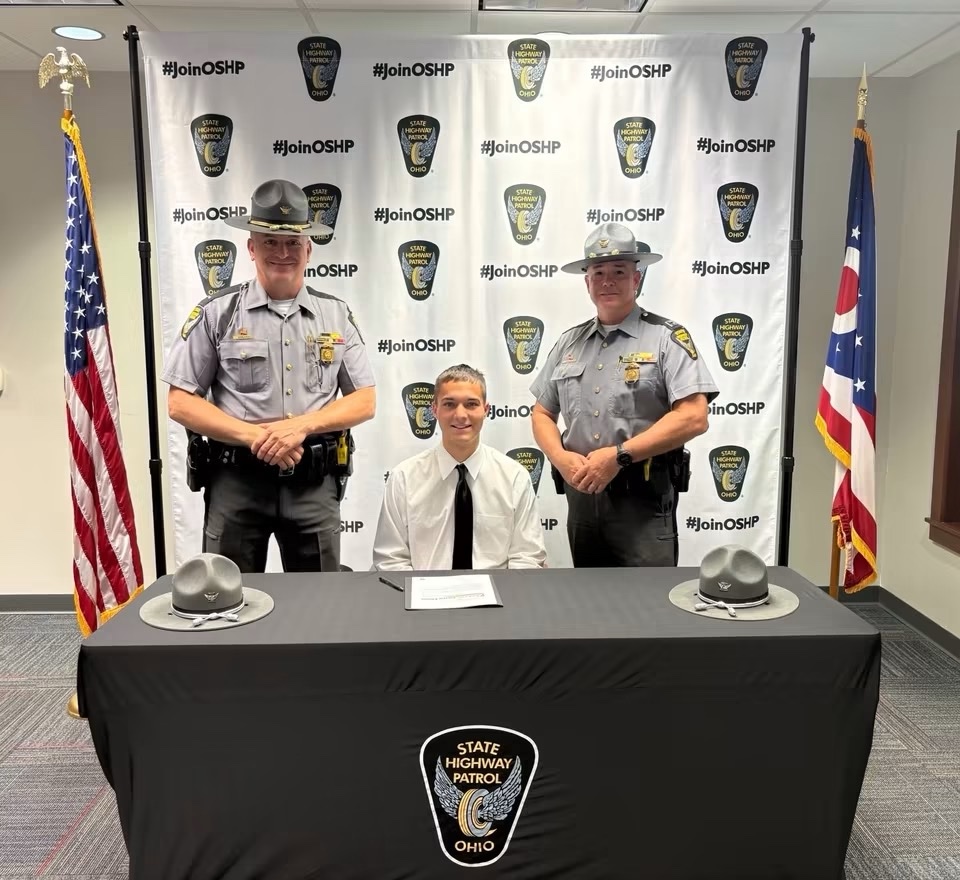 A cadet seated at the signing table between two Ohio State Highway Patrol troopers