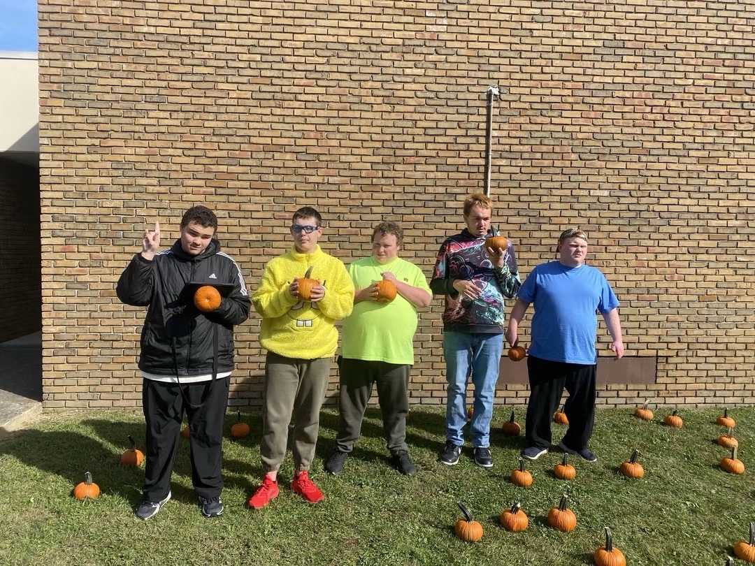 Five students standing in the pumpkin patch holding pumpkins