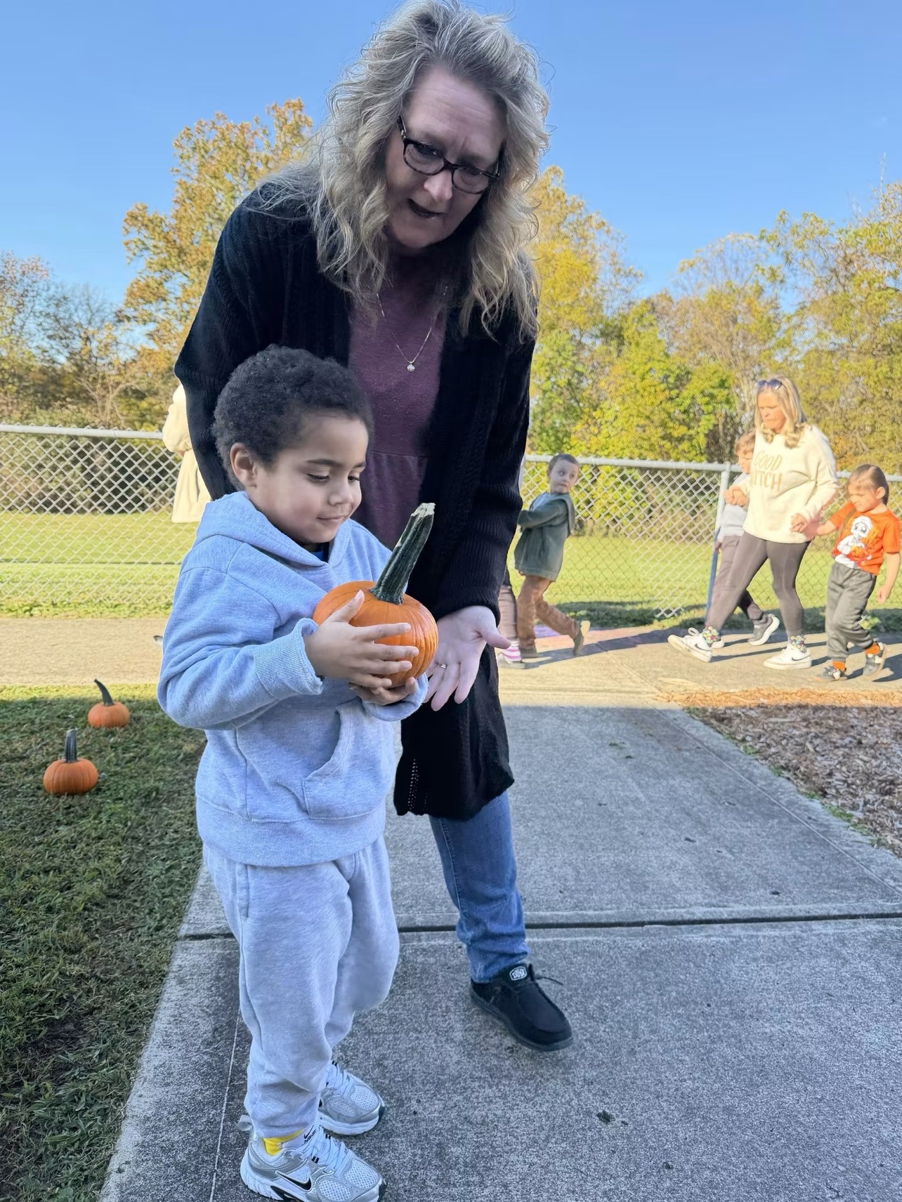 A young student holding a pumpkin next to a teacher